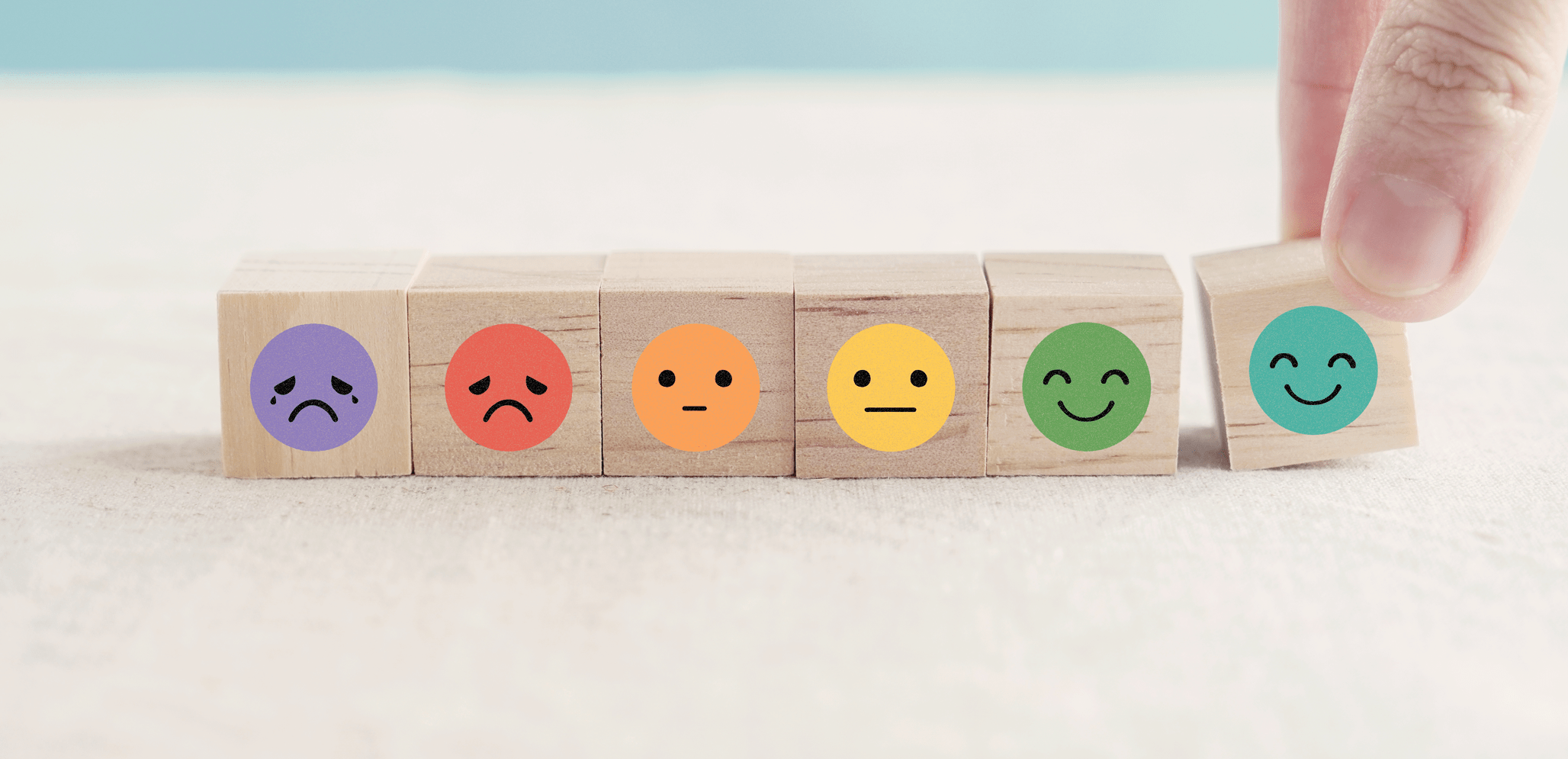 small wood blocks with colorful face emojis showing range of emotions from anger to happy.