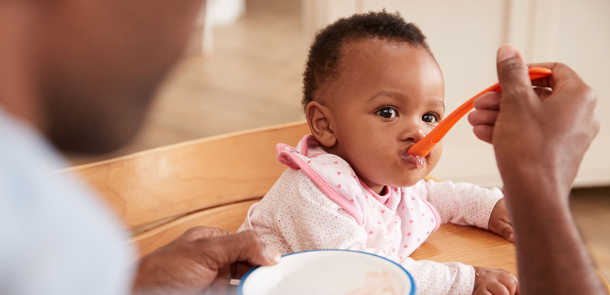 person spoon-feeding baby food to infant.