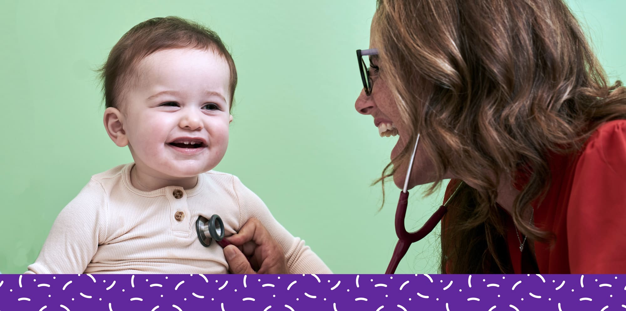 Pediatrician Kristen Terrill holding stethoscope to listen to chest of smiling toddler.